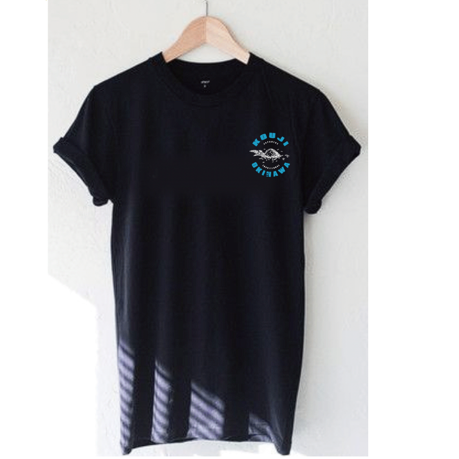 仲宗根糀家のオリジナルTシャツ：木のハンガーに掛けた黒いTシャツ、左胸に青い「KOUJI OKINAWA」の丸いロゴ