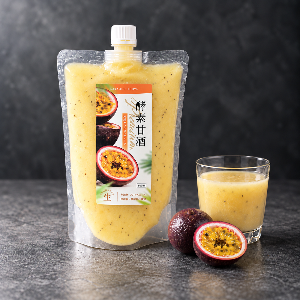 黒い石の台に置いた酵素甘酒 Premium 沖縄パッションフルーツのパウチと、グラスに注いだ淡い黄色の甘酒、丸ごとと半分に切ったパッションフルーツ