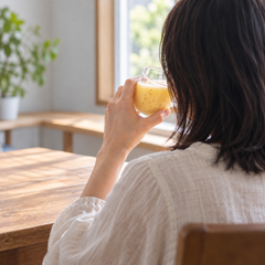 窓辺の木のテーブルで、グラスの甘酒を口もとへ運ぶ人の後ろ姿