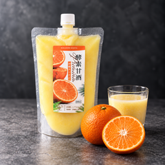 黒い石の台に置いた酵素甘酒 Premium 沖縄タンカンのパウチと、グラスに注いだ淡い黄色の甘酒、丸ごとと半分に切ったタンカン